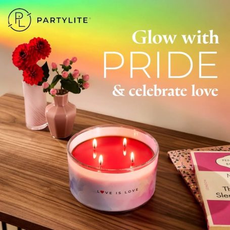A decorative candle with a rainbow design beside colourful flowers and a magazine on a table.