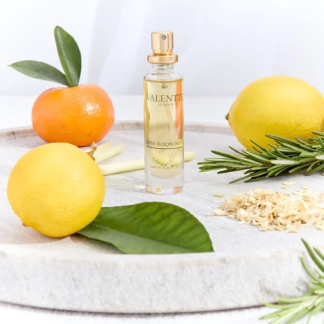 Valentte Room Mist A fragrance bottle surrounded by citrus fruits, rosemary, and a wooden surface.