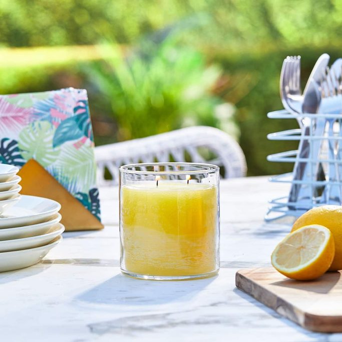 A glass of yellow drink with lemon, plates, and cutlery on a table outdoors.